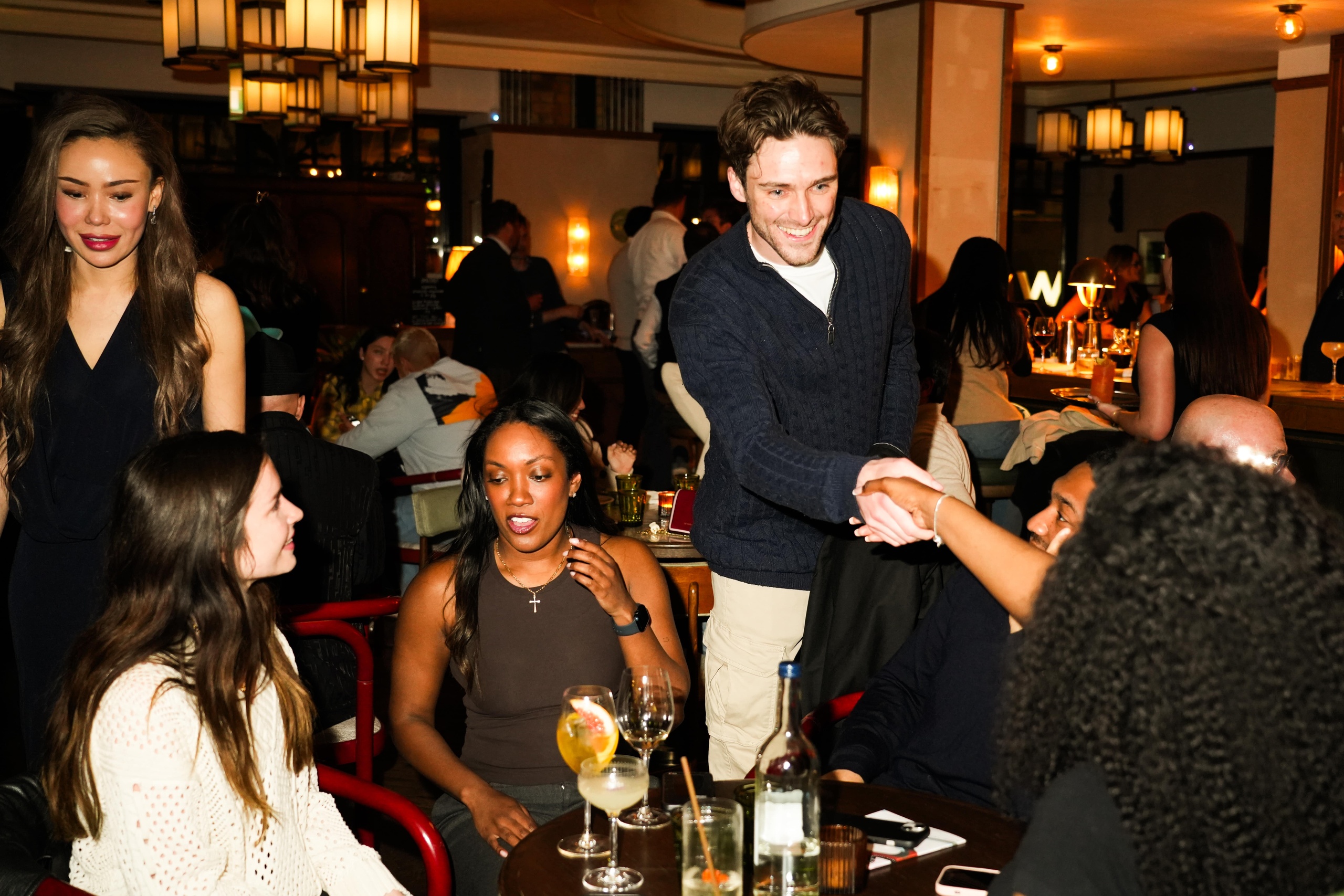 Group of people socialising at Nessa restaurant in Soho, with a man smiling and shaking hands during a lively evening gathering