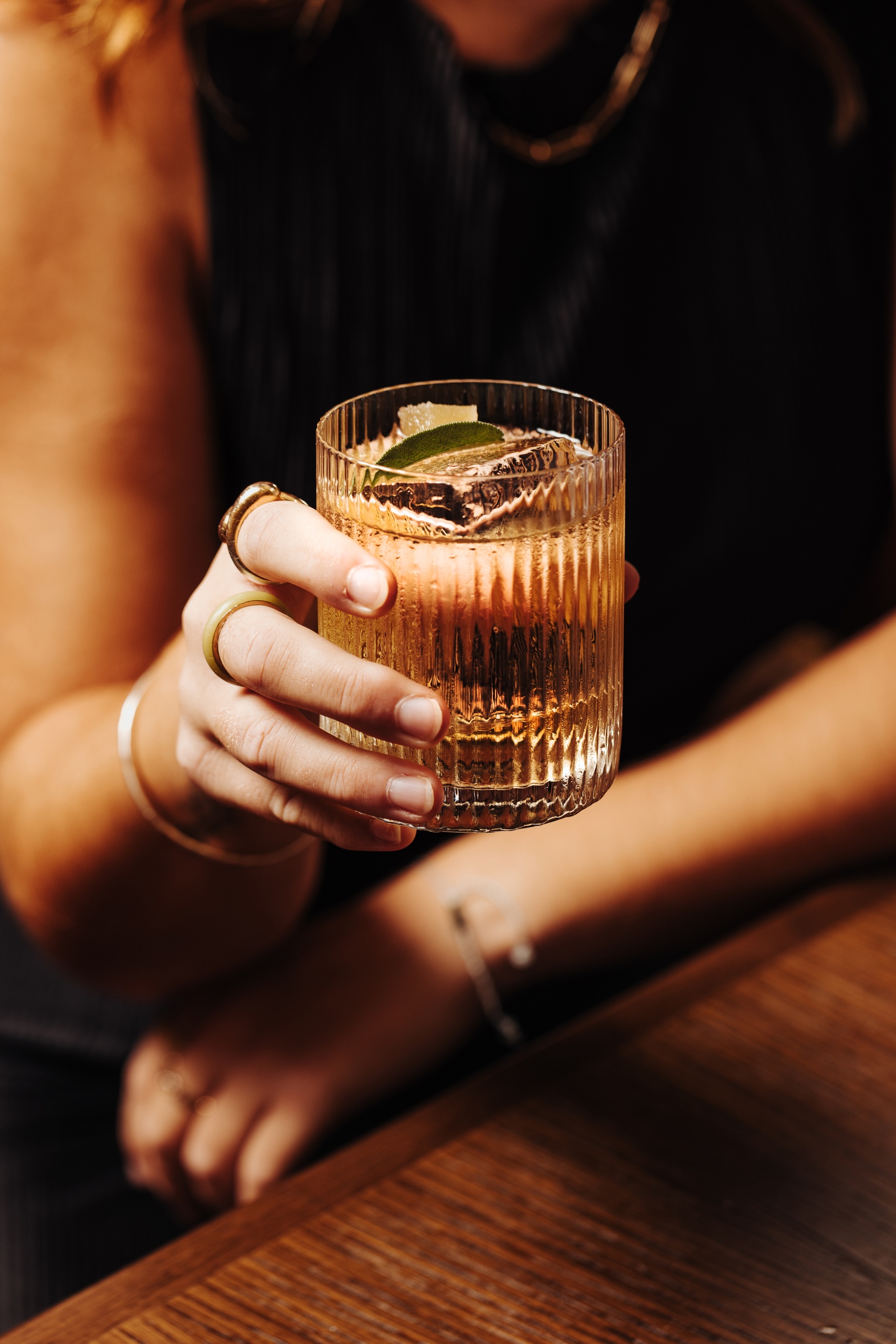 Close-up of a woman’s hand holding a cut-glass cocktail garnished with citrus and herbs at Nessa restaurant in Soho