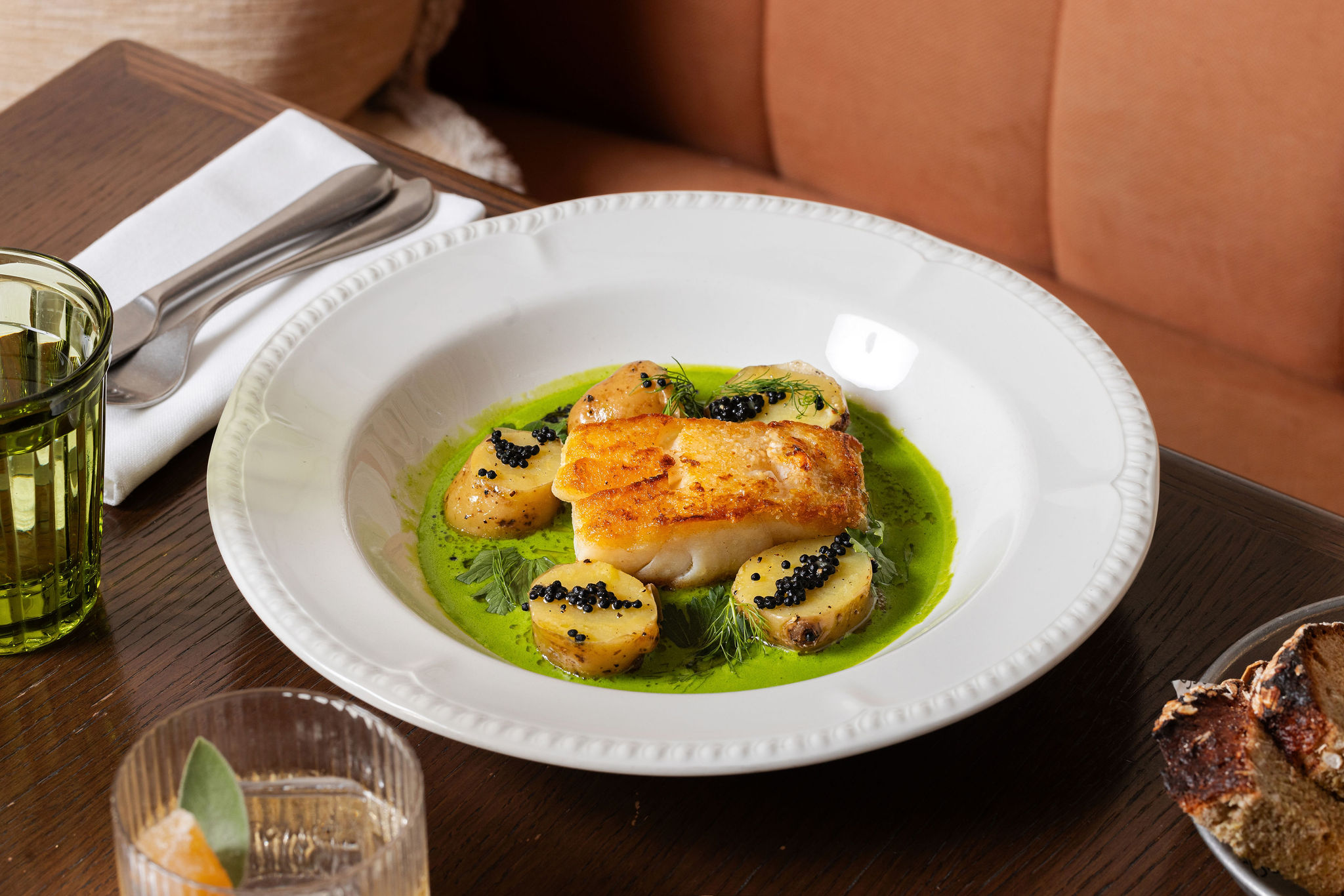 Plated pan-roasted cod with baby potatoes, caviar, and green herb broth on a white dish at Nessa restaurant in Soho