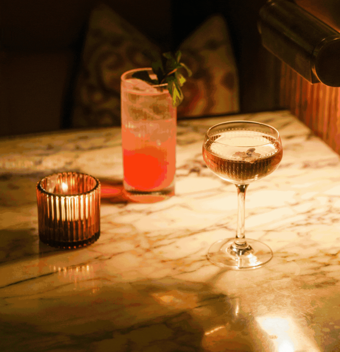 Animated gif of two signature cocktails and a lit candle on a marble bar table at Nessa restaurant in Soho