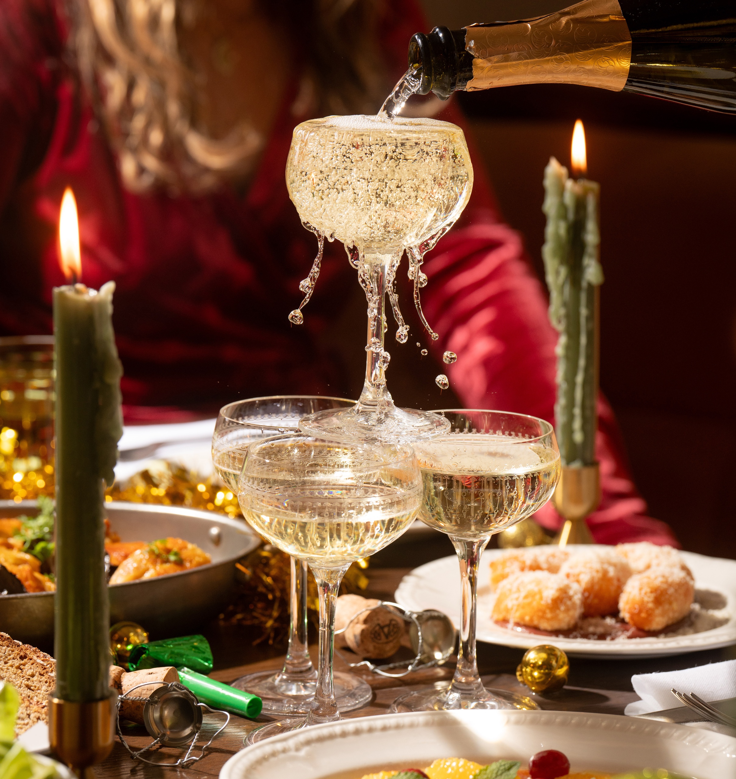 Champagne being poured into a tower of coupe glasses surrounded by festive food, candles, and golden holiday decor at Nessa restaurant in Soho