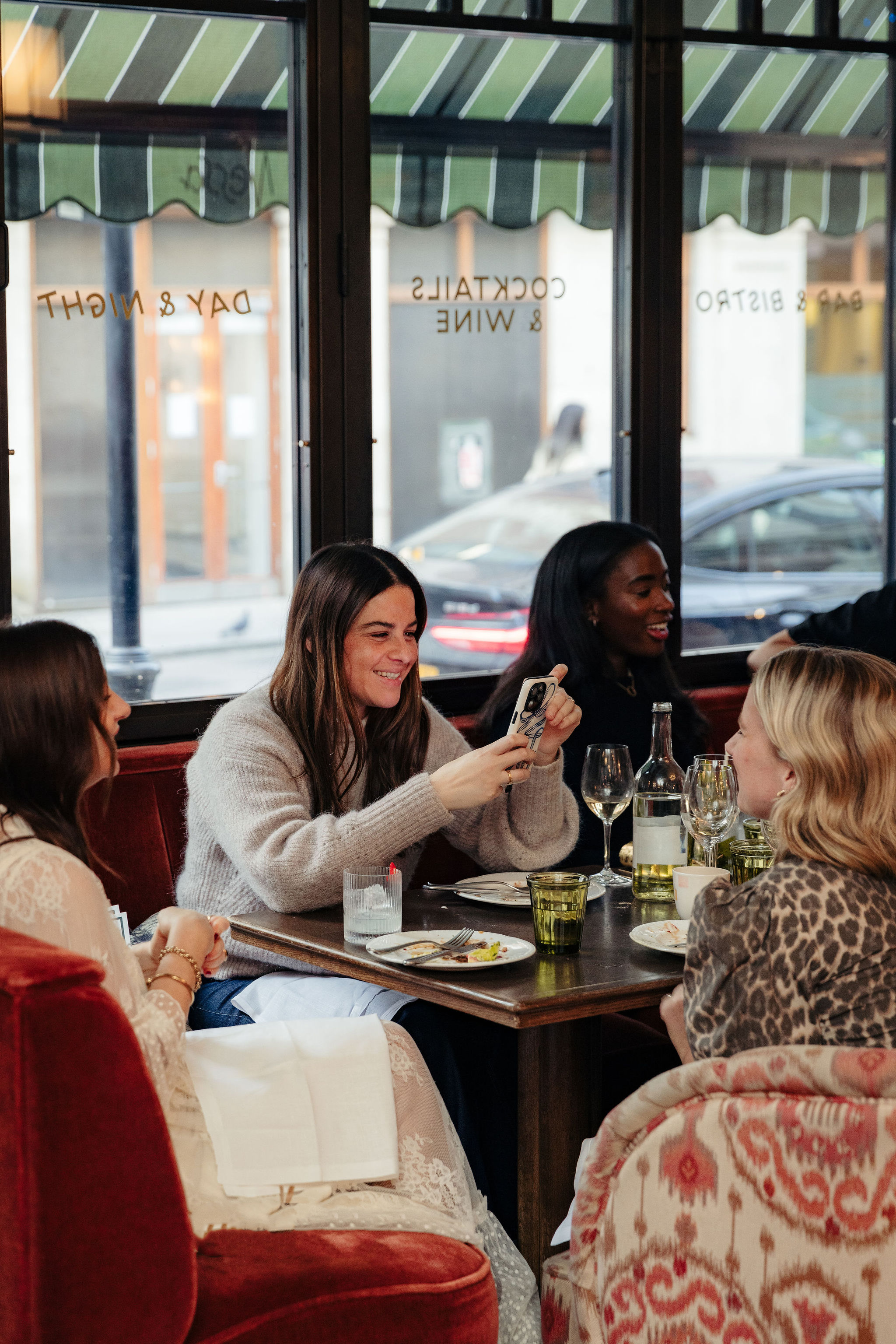 Group of women laughing and chatting at a Nessa restaurant table, one taking a photo with her phone